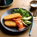 Plate of food with smoked salmon, avocado, and greens on a wooden table.