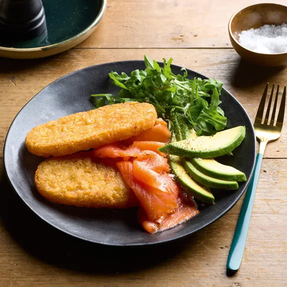 Plate of food with smoked salmon, avocado, and greens on a wooden table.