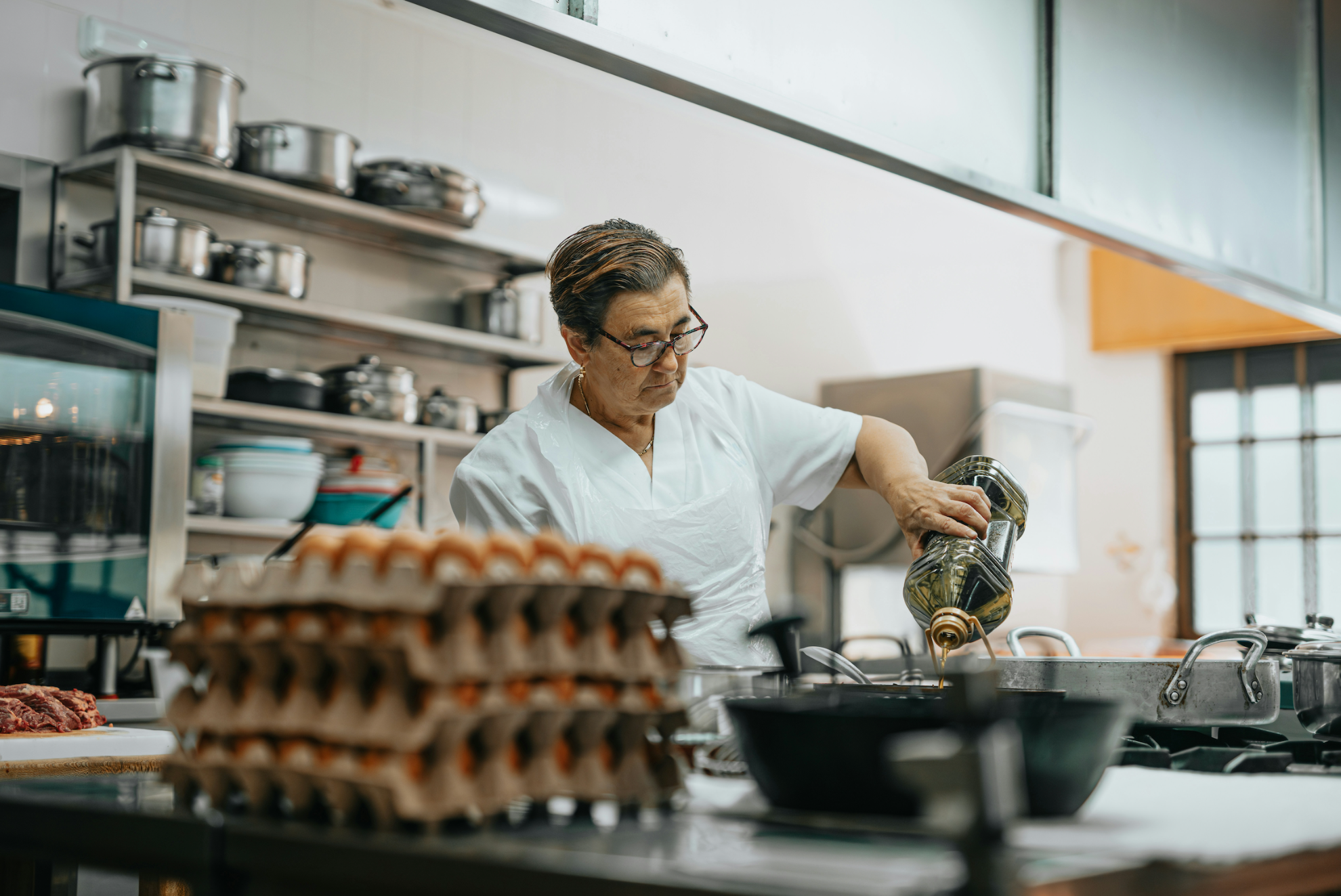 Person in a kitchen preparing food, with shelves and equipment in the background.