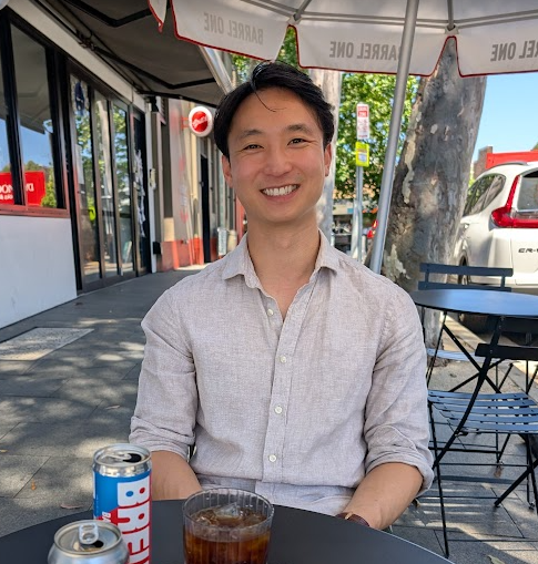 Man sitting at an outdoor cafe table with a can of soda and a glass, smiling.