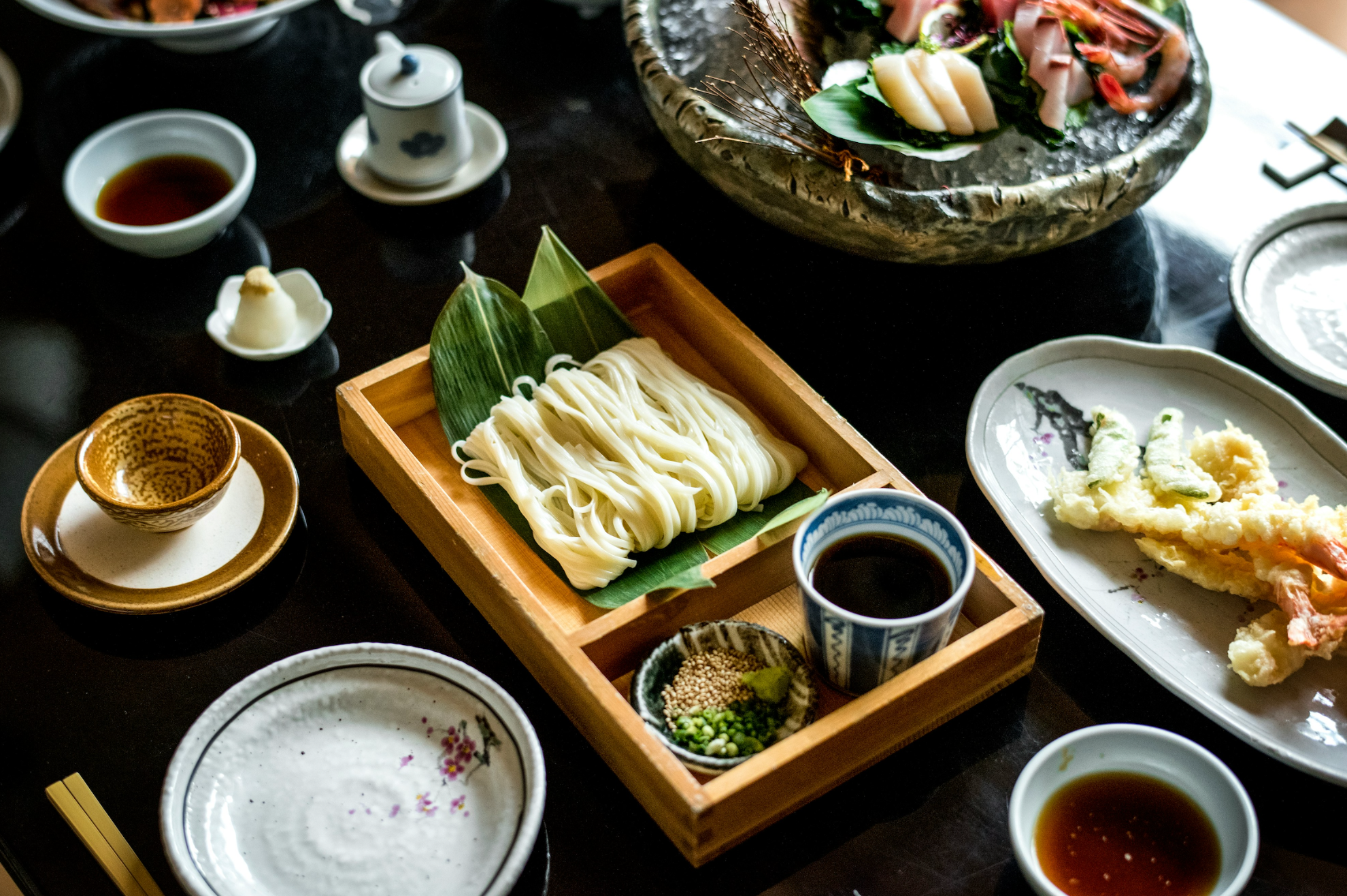 Japanese meal with noodles, tempura, and various condiments on a wooden tray.