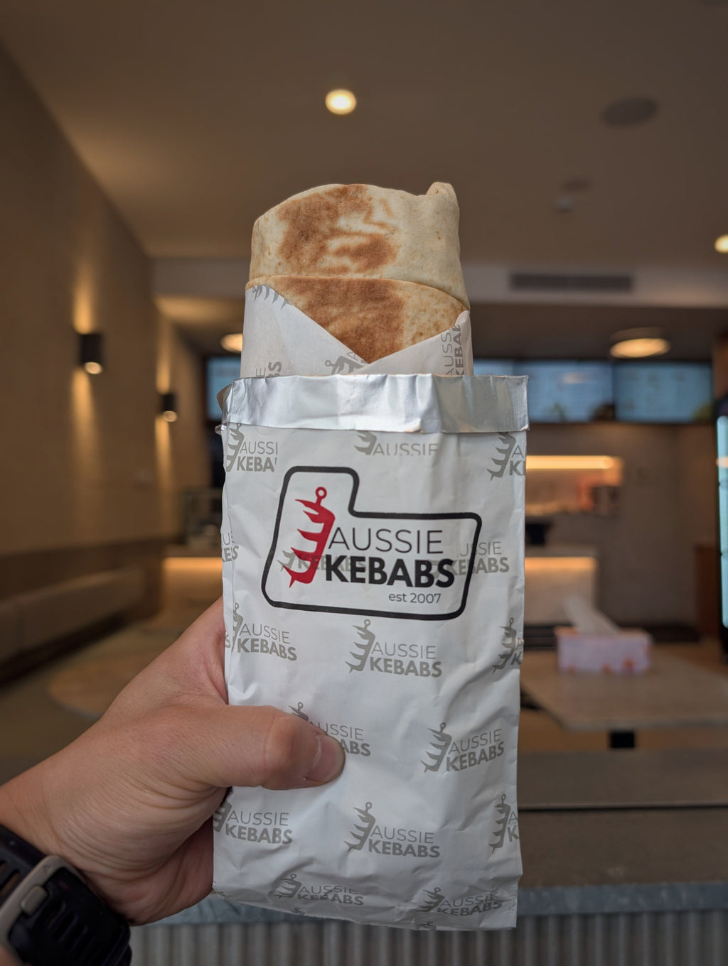 Aussie Kebabs wrap with a kebab held in a hand against an indoor background