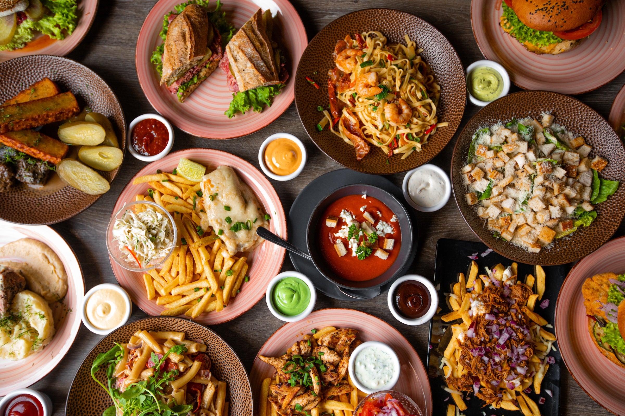 Assorted plates of food including sandwiches, fries, and salads on a wooden table.